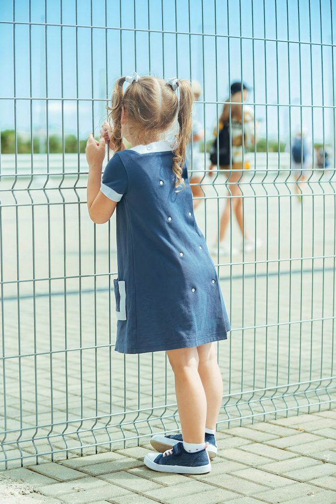 a little girl stands in front of a large mesh fence in a public place